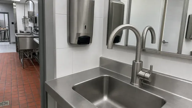 Stainless steel bathroom faucet in a food service facility staff restroom adjacent to commercial kitchen