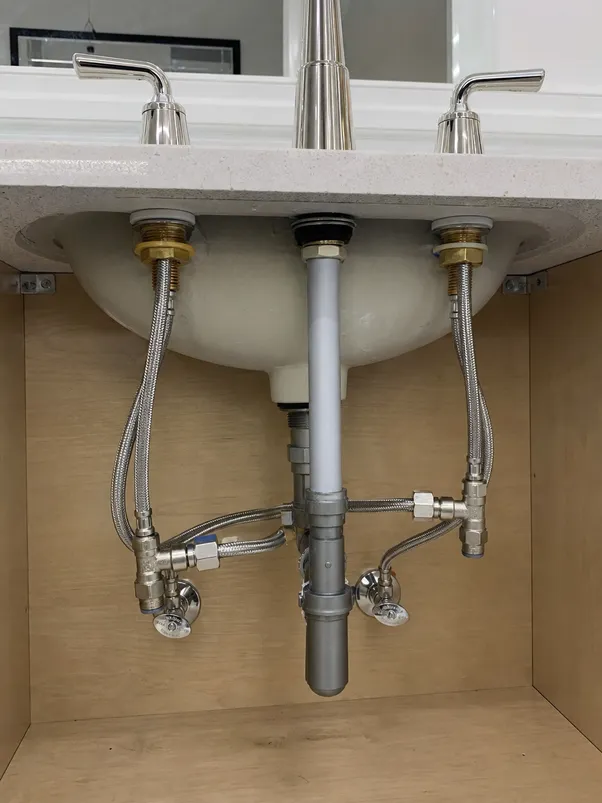 Under-sink view of two handle bathroom faucet installation showing supply line connections and mounting hardware