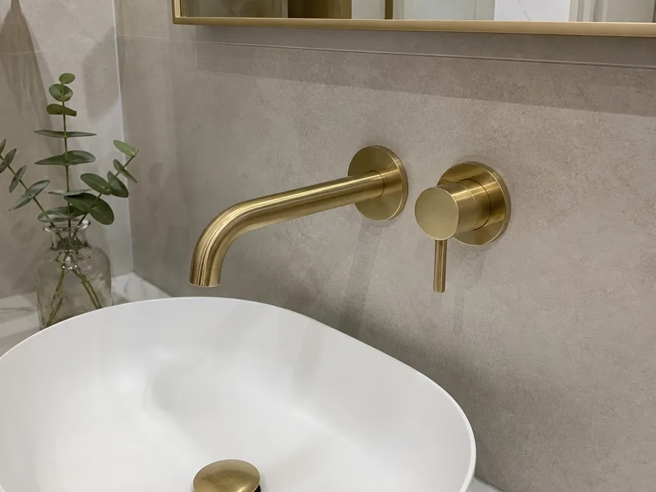 Brass wall mount bathroom faucet installed on tiled wall above vessel sink
