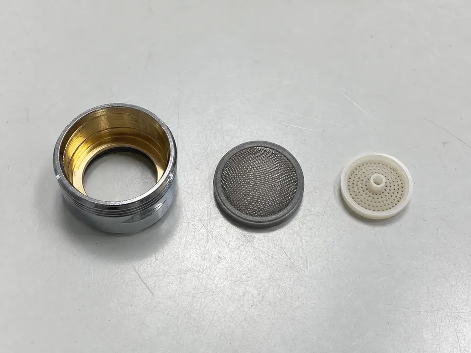 Faucet aerator components — brass housing, stainless mesh, and flow restrictor disc laid out for inspection