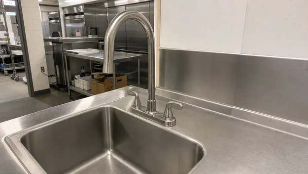 Stainless sink faucet in deck-mount configuration paired with stainless steel sink for commercial kitchen